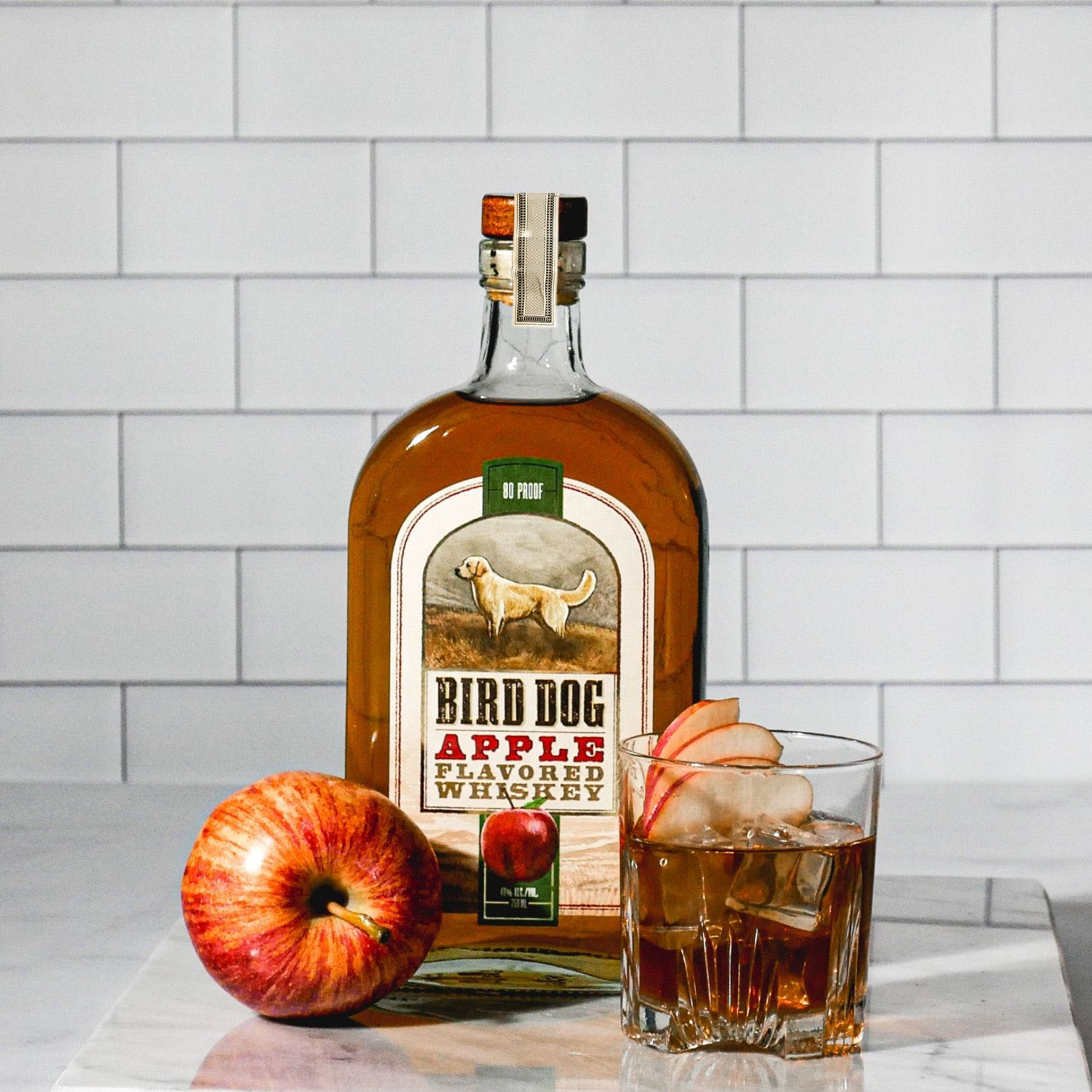 Bottle of Bird Dog Apple Whiskey Next to a Cocktail and Apple