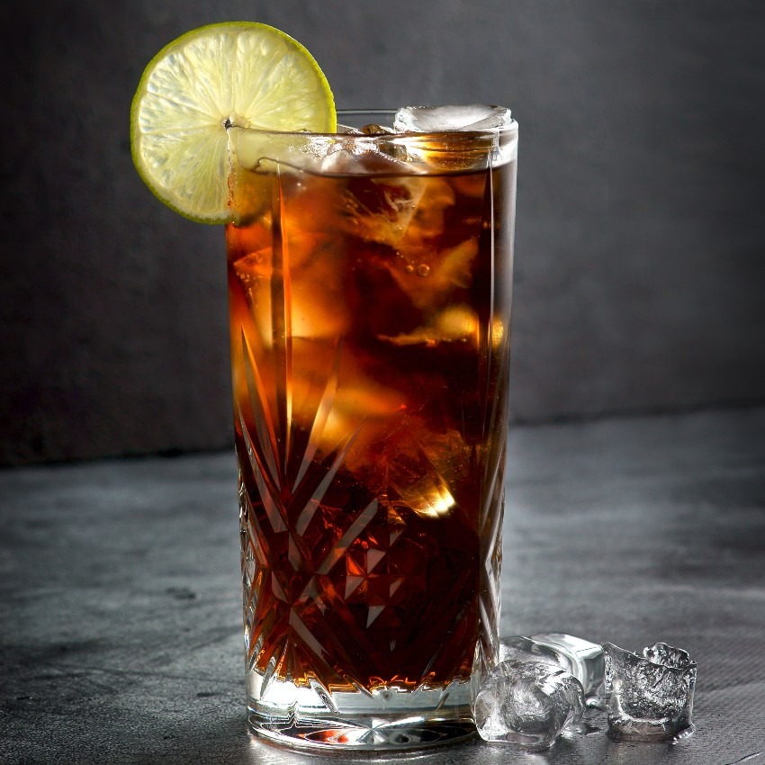 tall glass with Bird Dog's Mesquite Brown Sugar cola with ice and lime garnish