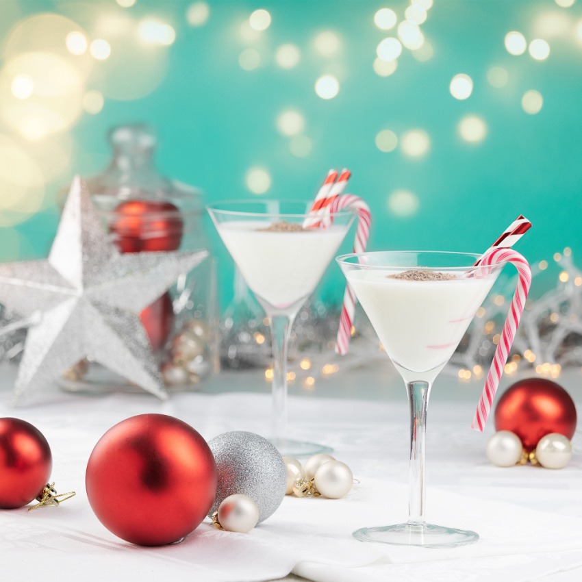2 martini glasses containing Bird Dog Candy Cane cocktail surrounded by Christmas decorations
